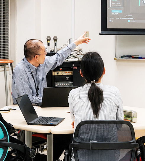 スクリーンを使って学生に説明するスタッフ