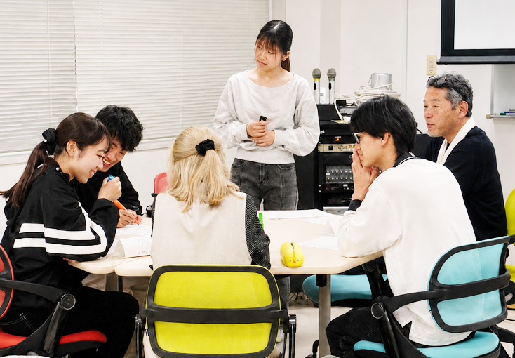 机を囲んでグループワークに取り組む学生とスタッフ